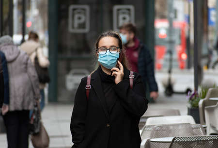 Vilnius, Lithuania - November 6 2020: Girl with phone wearing glasses and mask and walking in the city near a shop or shopping center during Covid or Coronavirus outbreakのeditorial素材