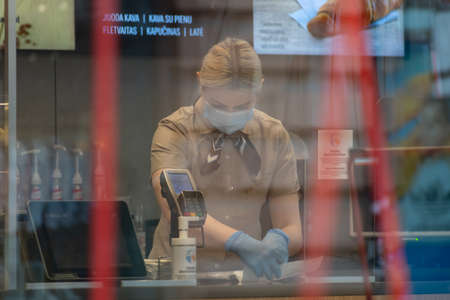 Young Caucasian blond girl with protective mask and gloves working in a shop, restaurant, fast fooのeditorial素材