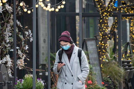 Vilnius, Lithuania - November 10 2020: Girl with mask walking and checking the app Stop Covid on the smartphone in the street during Covid or Coronavirus emergency, tracing app, tracking, Christmasのeditorial素材