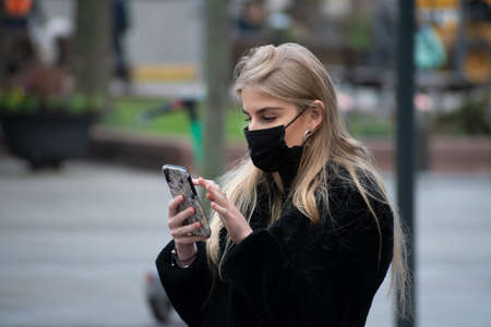 Vilnius, Lithuania - November 10 2020: Girl with mask walking and checking the app Stop Covid on the smartphone in the street during Covid or Coronavirus emergency, tracing app, tracking, Christmasのeditorial素材