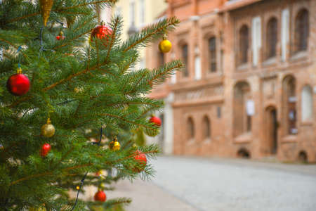 Close up details of real decorated Christmas tree with red and golden balls, old town on backgroundの写真素材