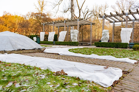 Plants and trees in a park or garden covered with blanket, swath of burlap, frost protection bags or...