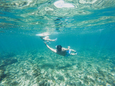 Child or kid swimming and diving in the sea or lake underwater with life or saver buoy and father or adult teaching in summerの写真素材