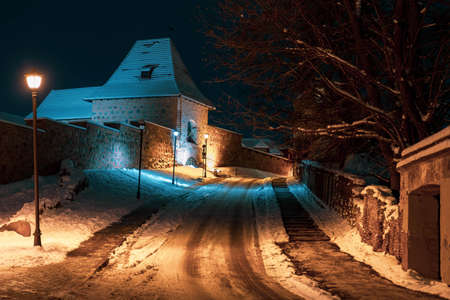 Bastion of Vilnius medieval defensive wall in Vilnius Old Town, evening or night view with old buildings and street lamp in winter with snowの写真素材