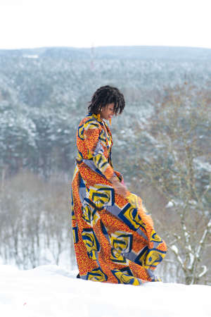 Beautiful girl with colorful dress walking on the snow in winter with forest trees covered by snow on background, verticalのeditorial素材