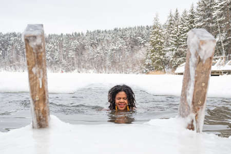 Beautiful girl swimming in the cold water of a lake or river, cold therapy, ice swim with winter landscape and forest on background, verticalのeditorial素材