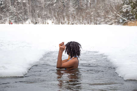 Beautiful girl swimming in the cold water of a lake or river, cold therapy, ice swim with winter landscape and forest on backgroundの写真素材