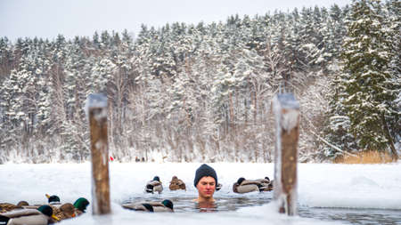 Vilnius, Lithuania - February 11 2021: Beautiful boy out focus bathing and swimming in the cold water of a lake or river among the ducks, cold therapy, ice swim with forest trees on backgroundのeditorial素材