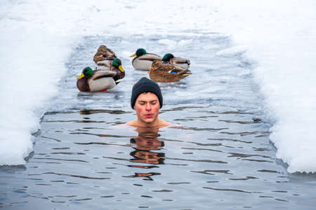 Vilnius, Lithuania - February 11 2021: Beautiful boy out focus bathing and swimming in the cold water of a lake or river among the ducks, cold therapy, ice swim with forest trees on backgroundのeditorial素材