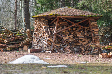 Circular or cylindrical structure or stack composed of blocks, pieces or logs of wood and roof in winter or spring with snow. The art of stacking wood for drying and storage in northern Europeの写真素材