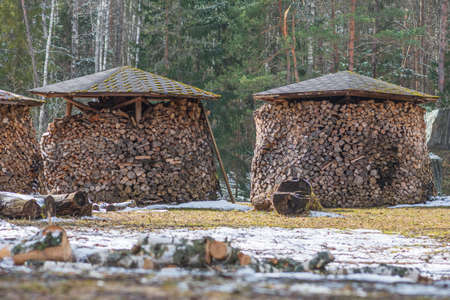 Circular or cylindrical structure or stack composed of blocks, pieces or logs of wood and roof in winter or spring with snow. The art of stacking wood for drying and storage in northern Europeの写真素材