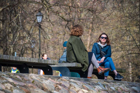 Vilnius, Lithuania - March 28 2021: Couple of women sitting and chatting without mask on a bench in a city park during pandemic restrictionsのeditorial素材
