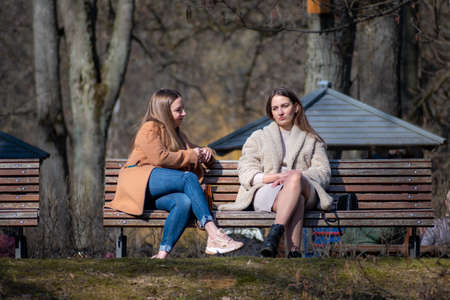 Vilnius, Lithuania - March 28 2021: Couple of beautiful young girls without mask sitting and chatting on a bench in a city park during pandemic restrictionsのeditorial素材
