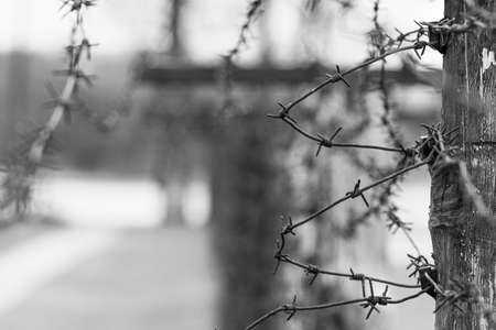 Close-up of a rusty barbed wire fence surrounding a concentration and extermination camp, focus in the background, black and whiteの写真素材