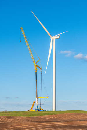 Wind turbine under construction near a village in a agricultural field with clear blue sky on background. Renewable energy concept, green ecological energy generation. Energy industry. Verticalの写真素材