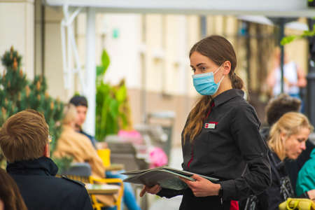 Vilnius, Lithuania - May 17 2021: Pretty nice waitress with mask and menu serving clients at the...