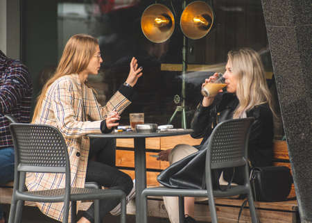 Vilnius, Lithuania - May 17 2021: Two beautiful girls without masks sitting and drinking coffee at an outdoor bar, cafÃ© or restaurant after quarantine restrictionsのeditorial素材