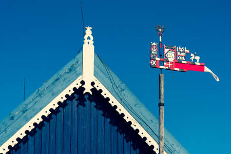 Beautiful colorful weathercock waving in the Curonian Spit in Nida fishermen's village, Lithuania, Europe with blue sky and roof of a wooden houseの写真素材