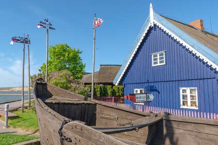 Nida, Lithuania - May 23 2021: Fisherman's museum. Beautiful old Lithuanian traditional wooden blue houses with thatched roof and old boat of the Curonian Spit in Nida fishermen's village, Lithuaniaのeditorial素材