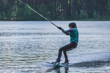 Vilnius, Lithuania - June 8 2021: Girl with helmet and life vest rides a wakeboard on the lake with...