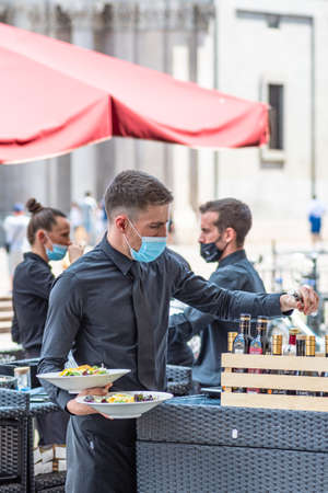 Torino, Italy - July 10 2021: Young nice waiter with mask preparing and serving food at an outdoor bar, cafÃ© or restaurant in the city during Covid or Coronavirus emergency, verticalのeditorial素材