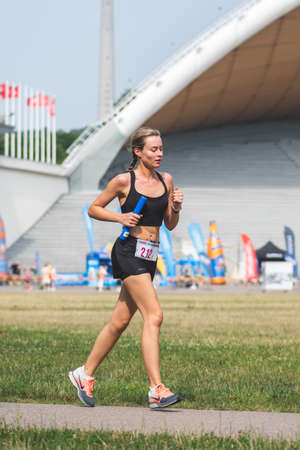 Vilnius, Lithuania - July 17 2021: Beautiful blond girl in sport clothes running in the park during a competition, verticalのeditorial素材