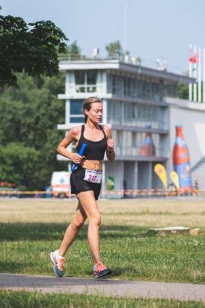 Vilnius, Lithuania - July 17 2021: Beautiful blond girl in sport clothes running in the park during a competition, verticalのeditorial素材