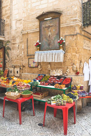 View of a narrow street in Bari old town, Puglia, Italy, traditional open fruit market shop with religious images and various local fruit and vegetables, verticalのeditorial素材