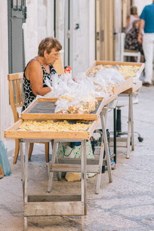 Bari, Italy - August 27 2021: Local elderly woman preparing in the street of Bari old town orecchiette or orecchietta, made with durum wheat and water, handmade pasta typical of Puglia, verticalのeditorial素材