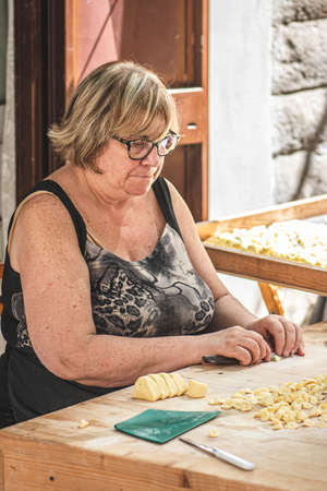 Bari, Italy - August 27 2021: Local elderly woman preparing in the street of Bari old town orecchiette or orecchietta, made with durum wheat and water, handmade pasta typical of Puglia, verticalのeditorial素材