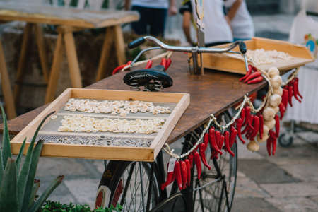 Fresh orecchiette or orecchietta, made with durum wheat and water, drying on a wooden board on a bike with red chili and garlic, handmade pasta typical of Puglia or Apulia, a region of Southern Italyの写真素材