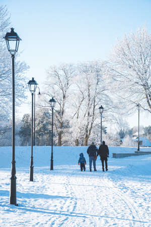 People walking in a white winter landscape with branches of tree covered by frost and snow, old street lamps and wooden houses, verticalの写真素材