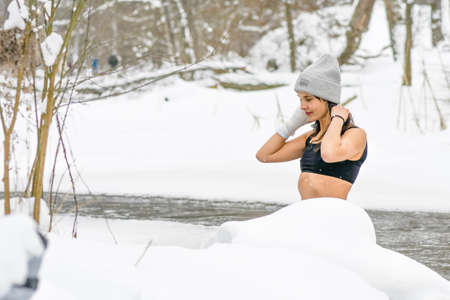 Vilnius, Lithuania - January 31 2021: Beautiful girl in the snow and enjoying winter in the cold water of a lake or river, cold therapy, ice swim with white winter landscape and forestのeditorial素材