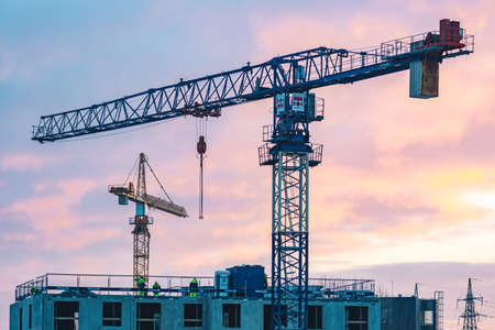 Vilnius, Lithuania - January 24 2022: Worksite with cranes, new buildings or houses under construction with workers with helmet at work and colorful sky in the backgroundのeditorial素材