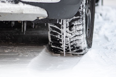 Close up winter tire of a car on the road covered by snow and ice driving in extreme cold...
