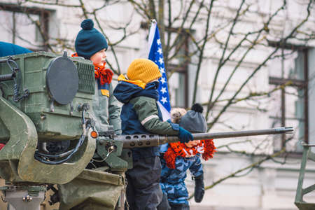 Vilnius, Lithuania - February 16 2022: Kids or children playing like soldiers on the top of a tank or military vehicle with a machine gun, with American flag on backgroundのeditorial素材