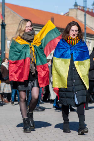 Vilnius, Lithuania - March 11, 2022: Peaceful demonstration against war, Putin and Russia in support of Ukraine, with a couple of friends with Ukrainian and Lithuanian flags together, verticalのeditorial素材