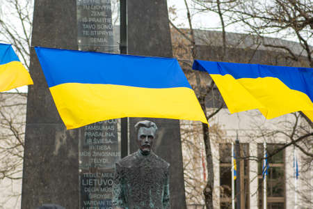 Vilnius, Lithuania - March 5 2022: Yellow and blue Ukrainian flags waving with Vincas Kudirka Square Monument in Vilnius, capital of Lithuaniaのeditorial素材