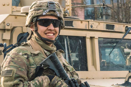 United States - March 29 2022: Smiling United States Marine Corps soldier with sunglasses, shotgun and armored vehicle humvee on background during war, USA or US army troopsのeditorial素材