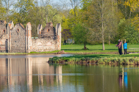 Preili, Latvia - May 14 2022: Preili Manor Complex, one of the most fabulous city parks in Preili, Latgale, Latvia surrounded by lake or pond, green landscape and people fishingのeditorial素材
