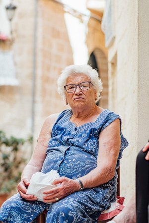 Bari, Puglia, Italy - July 10 2022: Elderly local woman sitting on a chair on the doorstep in the narrow streets of Bari old town, Puglia, Italy, verticalのeditorial素材
