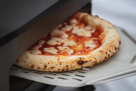 Cooking or baking hot pizza Margherita with tomato sauce and mozzarella cheese with a shovel in an electric or gas oven, with smoke, close upの写真素材