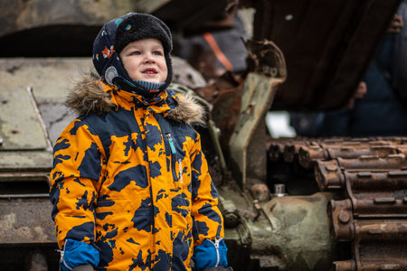 Kyiv, Ukraine - February 25 2023: Child photographed near a burnt and melted rusty wreckage of a Soviet Russian-made tank T-72B destroyed during the Russian invasion of Ukraine in a square in Kievのeditorial素材