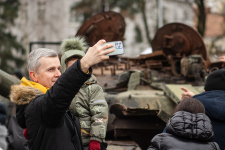 Kyiv, Ukraine - February 25 2023: Father and son taking a selfie near a burnt and melted rusty wreckage of a Soviet Russian-made tank T-72B destroyed during Russian invasion of Ukraine in Kievのeditorial素材