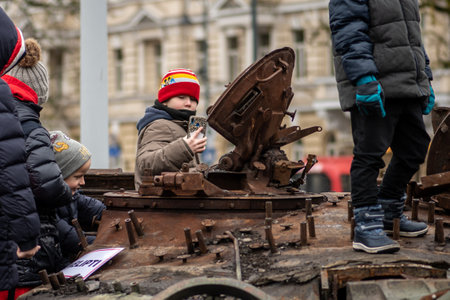Kyiv, Ukraine - February 25 2023: Children playing on a burnt and melted rusty wreckage of a Soviet Russian-made tank T-72B destroyed during the Russian invasion of Ukraine in a square in Kievのeditorial素材