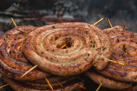Spiral-rolled sausages ready to eat, grilled or roasted in a barbecue on an open fire and flames, in a street food market or an outdoor picnic, close upの写真素材