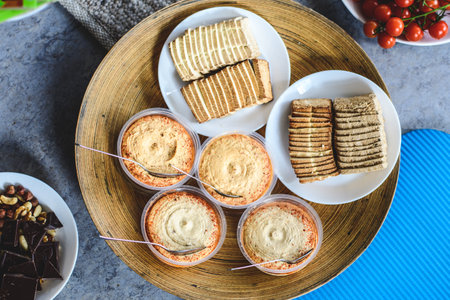 Vegan food, tofu, hummus served in a bamboo tray with a plate of chocolate, and dried fruit and a plate of cherry tomatoes aroundの写真素材