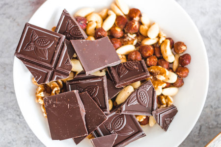 Chocolate with dried fruit, cashews, walnuts, hazelnuts in a white plate on the table, view from...