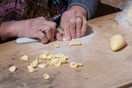 Wrinkled hands of an elderly woman preparing fresh orecchiette or orecchietta, made with durum wheat and water, handmade pasta typical of Puglia or Apulia, a region of Southern Itaの写真素材