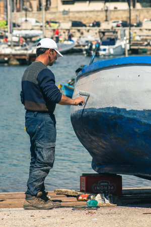 Bari, Puglia, Italy - April 8 2023: Fisherman repairing and painting an old wooden fishing boat at the port quay in Bari, Puglia Italyの写真素材